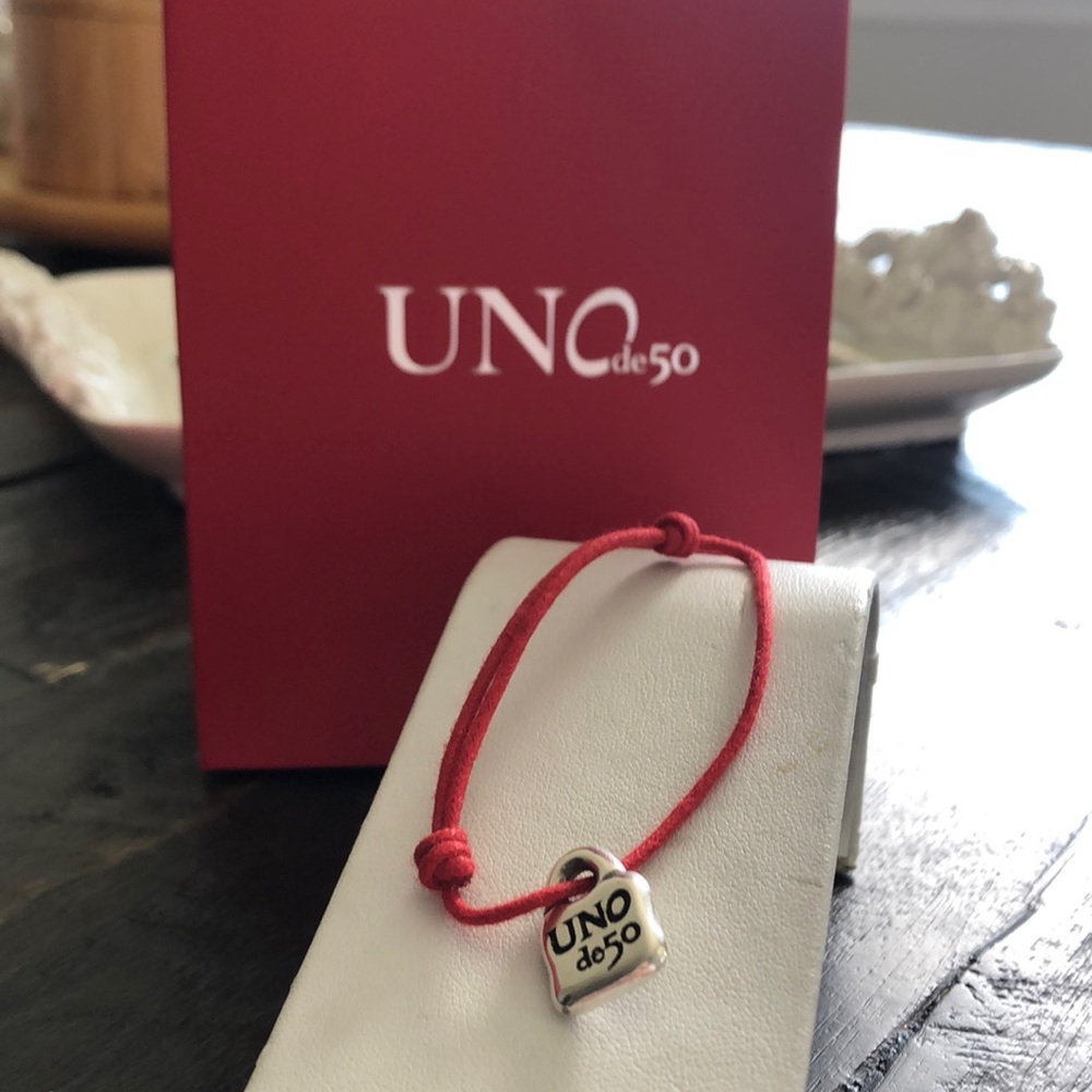 Adjustable red  bracelet with two knots and a silver-plated UNOde50  charm.